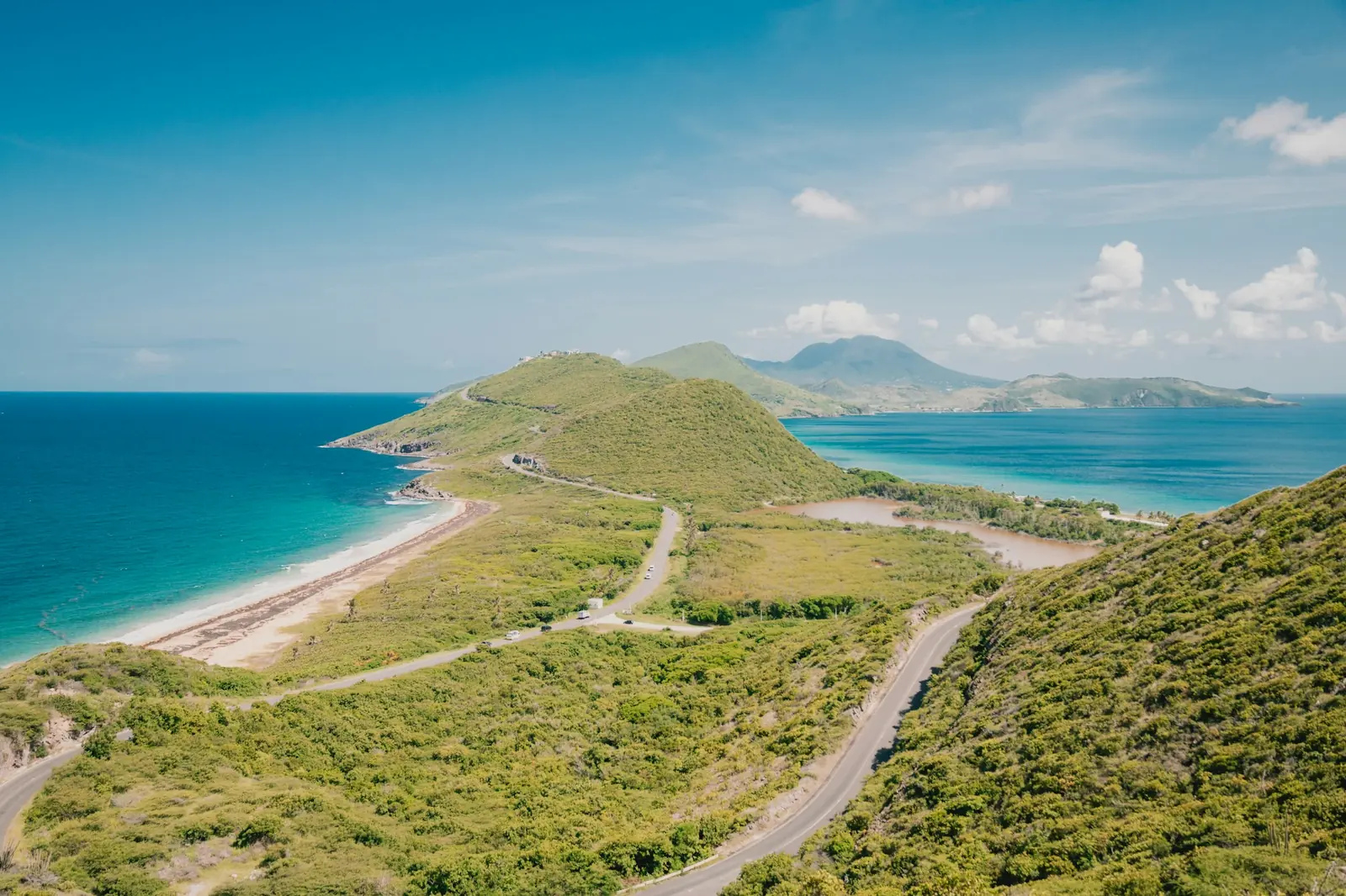A road winding over green hills of the South East Peninsula of St Kitts above the sea